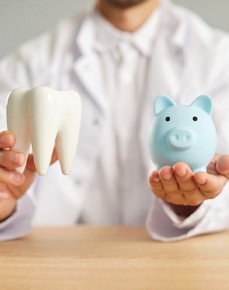 Dentist holding model tooth and blue piggy bank