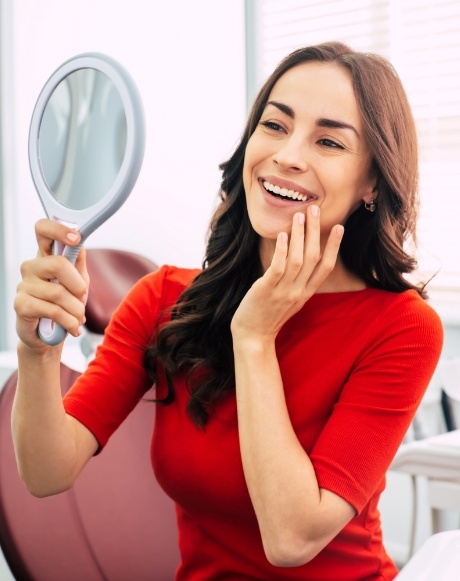 Woman with porcelain veneers looking at smile in mirror