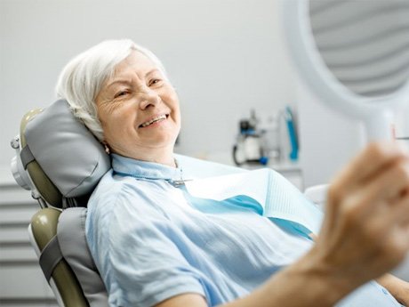 Senior woman using mirror to admire her new dentures
