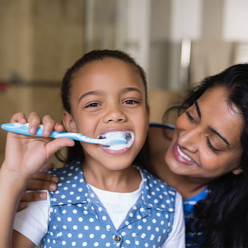 Mother helping child brush teeth to prevent dental emergencies