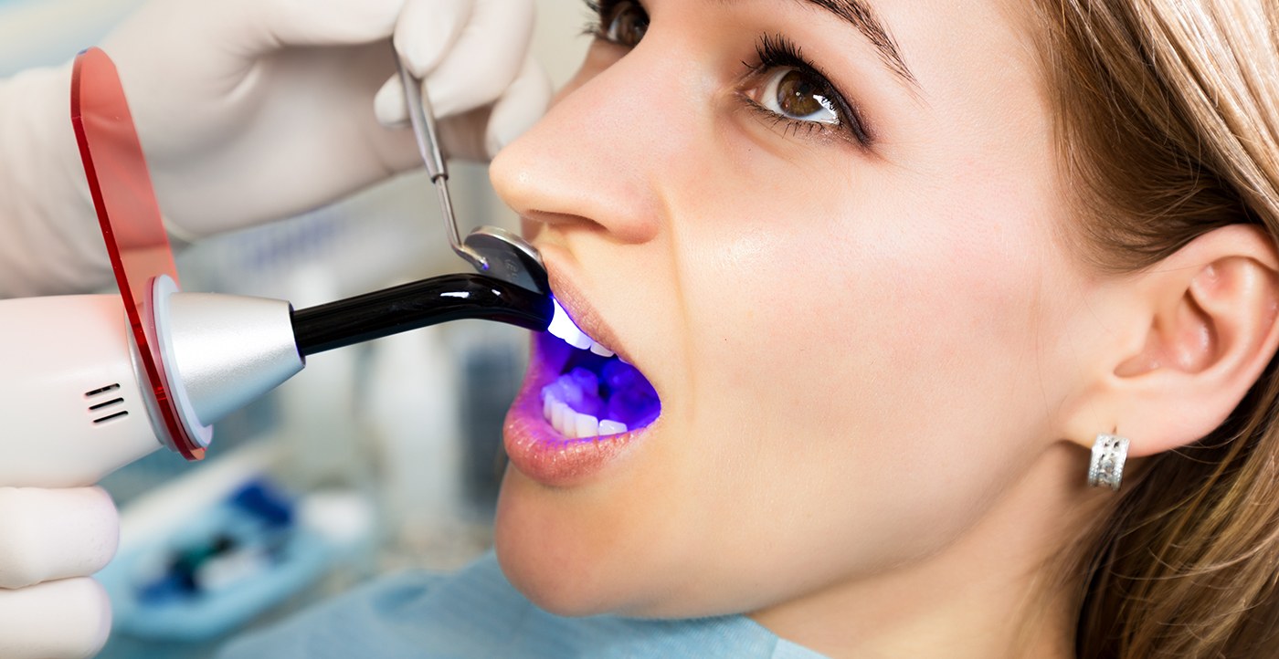 Dentist applying ultraviolet light to woman’s tooth to complete treatment