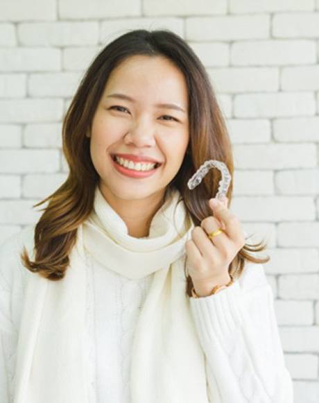 a woman smiling and holding Invisalign clear aligners