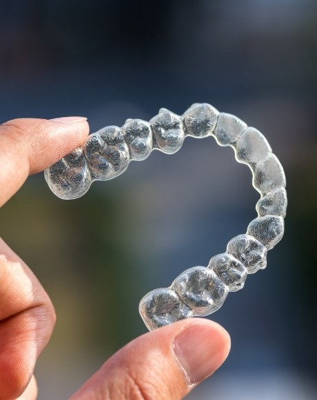 Hand holding an Invisalign clear braces tray