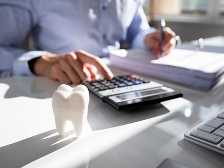Someone calculating costs at desk with model tooth