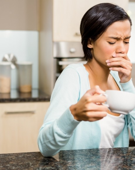 Woman wincing in pain after taking a drink of coffee